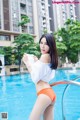 A woman in an orange bikini standing next to a swimming pool.