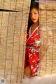 A woman in a red kimono is peeking out from behind a bamboo fence.