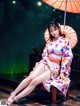 A woman in a kimono sitting on a bench under an umbrella.