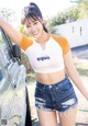 A woman in shorts and a t-shirt leaning against a car.