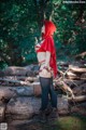 A woman in a red hooded outfit standing in the woods.