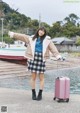 A woman standing next to a pink suitcase on a dock.