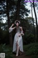 A woman in a white dress and hat standing in the woods.