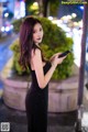 A woman in a black dress holding a cell phone.