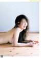 A naked woman laying on a wooden floor holding a flower.