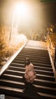 A woman crouching down on a set of stairs at night.